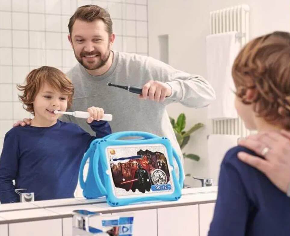 Isä ja poika harjaavat hampaita yhdessä, poika seuraa tabletista sähköhammasharjan käyttöopasta.